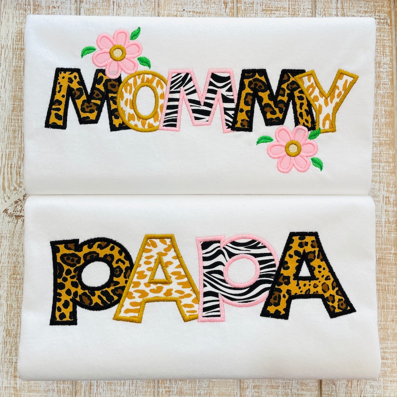 Peut inclure: Deux chemises blanches avec les mots "MOMMY" et "PAPA" brod&eacute;s en lettres d'imprim&eacute;s animaliers noirs, bruns et blancs. Des fleurs roses sont brod&eacute;es au-dessus du mot "MOMMY" et en dessous du mot "PAPA".