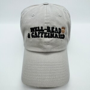 May include: A gray baseball cap with black embroidery that reads "Well-Read & Caffeinated" with a small brown coffee cup graphic.