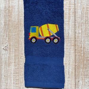 May include: A blue bath towel with an embroidered yellow cement mixer truck. The truck has a red cab and black wheels.