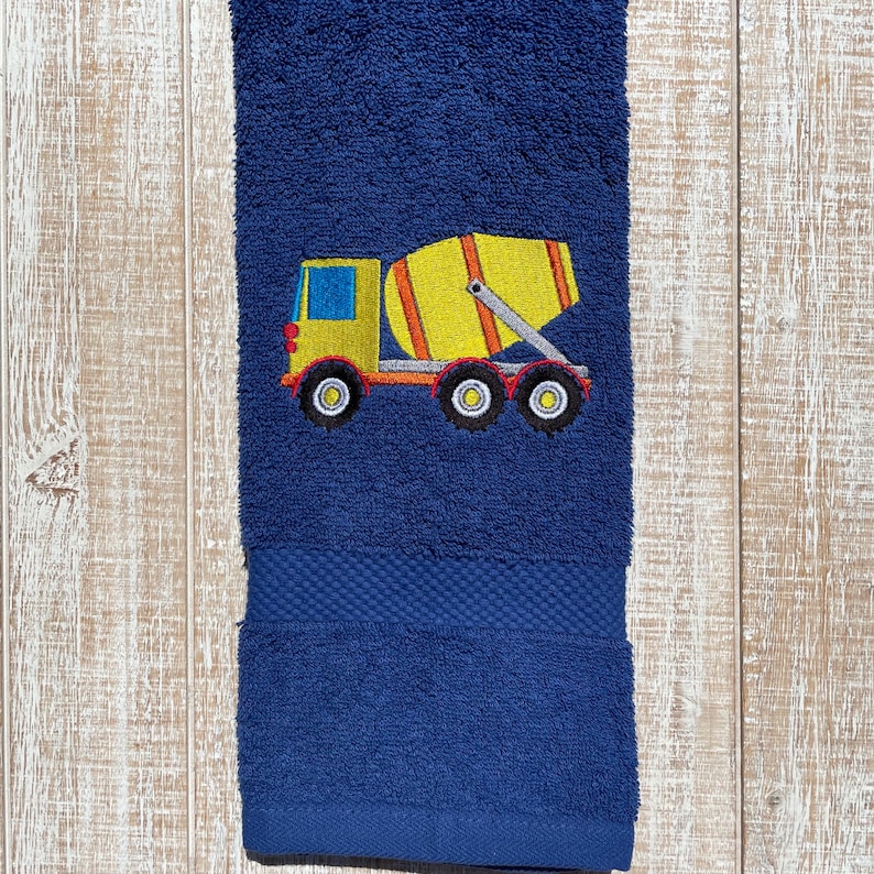 May include: A blue bath towel with an embroidered yellow cement mixer truck. The truck has a red cab and black wheels.