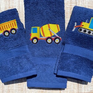 May include: Three blue hand towels with embroidered yellow construction vehicles. The towels feature a dump truck, a cement mixer, and a bulldozer.