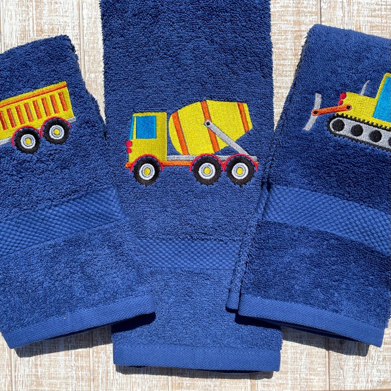 May include: Three blue hand towels with embroidered yellow construction vehicles. The towels feature a dump truck, a cement mixer, and a bulldozer.