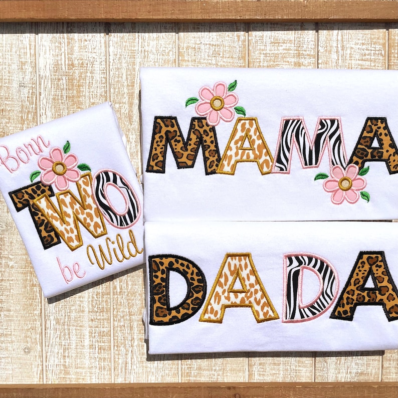 Peut inclure: Trois t-shirts blancs avec des lettres brod&eacute;es en imprim&eacute; animal qui &eacute;pellent "Born Two Be Wild", "Mama" et "Dada". Les lettres sont en tissu imprim&eacute; l&eacute;opard, gu&eacute;pard et z&egrave;bre. Chaque t-shirt a des fleurs roses.