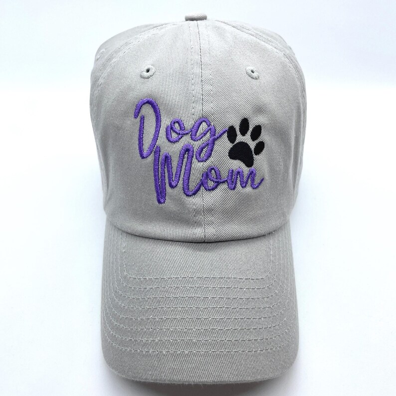 May include: A gray baseball cap with the embroidered text "Dog Mom" in purple script and a black paw print. The cap has a curved brim and an adjustable strap.