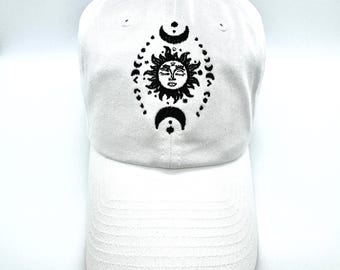 May include: White baseball cap with a black embroidered design of a sun and moon with a face.