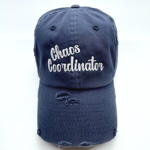 May include: A dark blue distressed baseball cap with the text "Chaos Coordinator" embroidered in white.