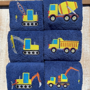 May include: Set of six blue towels with embroidered yellow construction vehicles. The vehicles include a crane, excavator, dump truck, cement mixer, and two bulldozers.