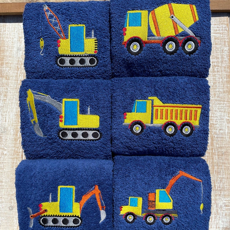 May include: Set of six blue towels with embroidered yellow construction vehicles. The vehicles include a crane, excavator, dump truck, cement mixer, and two bulldozers.