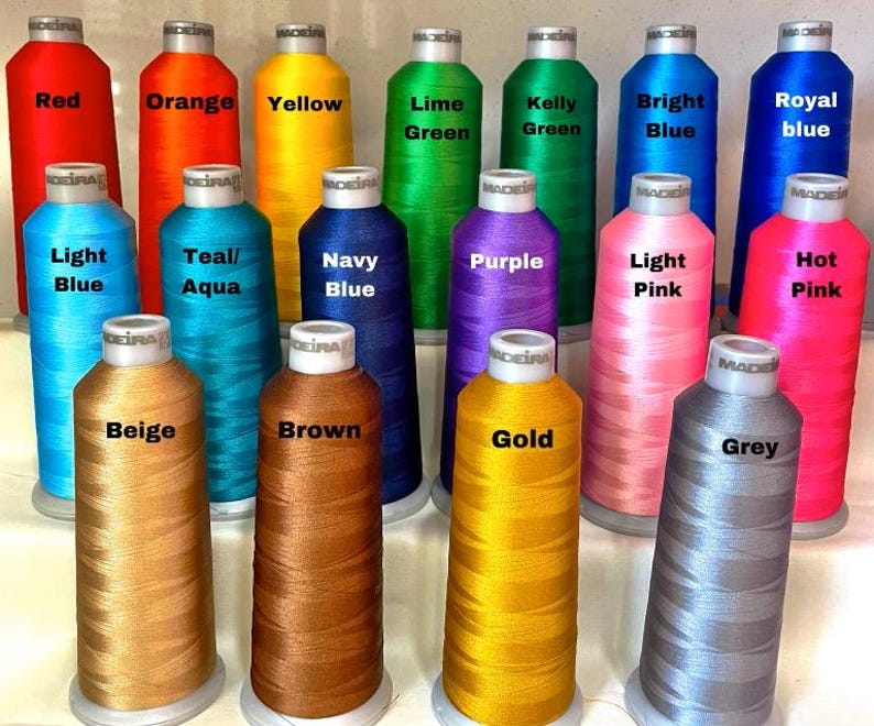 May include: A collection of colorful spools of thread, each labeled with a different color name. Colors include red, orange, yellow, green, blue, pink, and more. The spools are arranged in rows, showcasing a wide variety of shades.