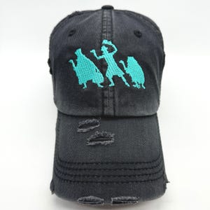 May include: Black distressed baseball cap with a turquoise embroidered design of three ghost figures.