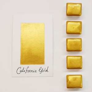 Puede incluir: Una tarjeta blanca con un rectángulo dorado y el texto manuscrito "California Gold" junto a cinco pequeñas muestras de pintura cuadradas de color dorado. La pintura tiene un acabado metálico y brillante.