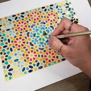 Op de afbeelding: Een kleurrijk geometrisch aquarel schilderij met gouden accenten. Het kunstwerk toont een herhalend patroon van sterren en andere vormen in tinten blauw, rood, geel en teal. Een hand houdt een gereedschap, mogelijk een stylus, boven het kunstwerk.