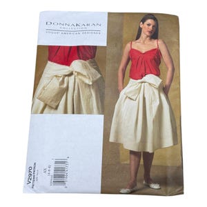 Pode incluir: Um envelope de molde de costura Donna Karan Collection Vogue American Designer V2970, tamanho AX (4-6-8). A capa apresenta um top vermelho sem mangas e uma saia plissada cor de creme, pelo joelho, com um grande laço na cintura.