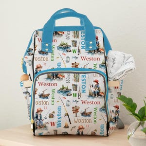 May include: A white and blue backpack with a fishing theme. The backpack features illustrations of a boy fishing, boats, fish, and fishing poles. The name "Weston" is printed throughout the design. The backpack has blue straps and a handle.