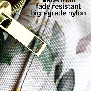 May include: Close-up of a section of a bag with a gold zipper and a floral pattern. The bag is made from fade-resistant, high-grade nylon. The zipper is open, revealing the interior.