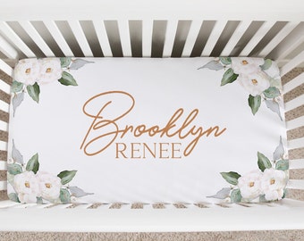 May include: White crib sheet with a floral design in the corners and the name "Brooklyn Renee" written in brown cursive lettering.