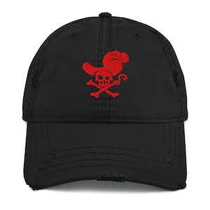 May include: Black distressed baseball cap with a red pirate-themed embroidered design. The design includes a skull, crossbones, and a pirate hat. The cap has a curved brim and an adjustable strap.