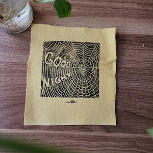 May include: A yellow fabric patch with a black spiderweb design and the text "Good Night" printed on it.