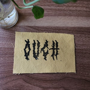 May include: A yellow fabric patch with the word "OUCH" embroidered in black.