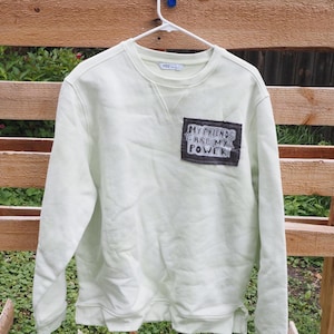 May include: A pale lime green long-sleeve sweatshirt featuring a rectangular black patch on the upper left chest. The patch contains the white hand-lettered text MY FRIENDS ARE MY POWER. The garment has a crew neckline and ribbed cuffs.