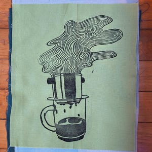 May include: A square piece of light green fabric featuring a black screen-printed illustration of a coffee dripper resting on a mug. The design depicts steam rising from the dripper in wavy, abstract lines, with coffee dripping into the glass mug.