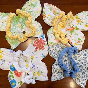 以下が含まれることがあります： 緑、オレンジ、ピンク、青、黄色の花柄が施された蝶の形の布製ウィング4点。各ウィングには、体に固定するための黄色、白、または青の無地の伸縮性のある布製ストラップが付いています。