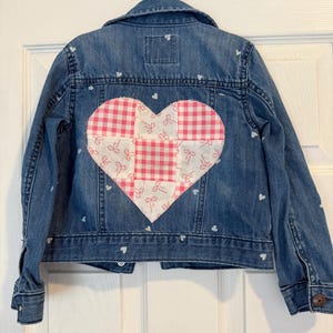 Jaqueta jeans infantil tamanho 5T, feita com jeans OshKosh reciclado e aplique de laço com patchwork de coração.