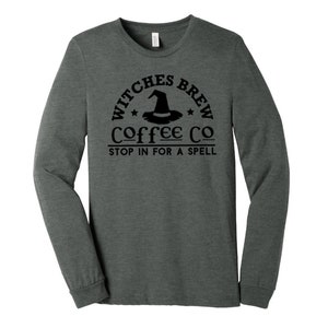May include: A dark heather grey long-sleeve t-shirt with a black graphic of a witch's hat and the text "Witches Brew Coffee Co. Stop in for a spell."
