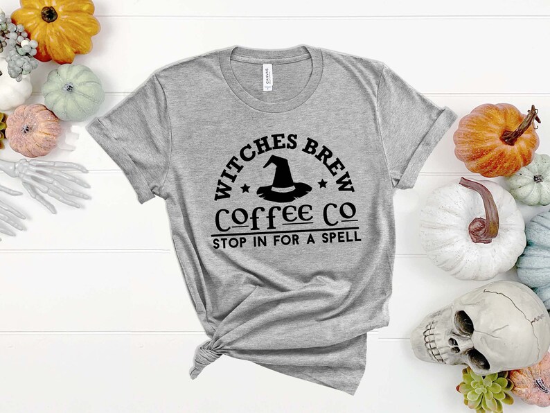 May include: A gray t-shirt with a black graphic that says "Witches Brew Coffee Co. Stop in for a spell". The graphic features a witch's hat with a star on each side.