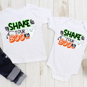 May include: Two white shirts with a ghost graphic and the text "Shake Your Boo-ty" printed on them. One shirt is a long-sleeved t-shirt and the other is a short-sleeved onesie.