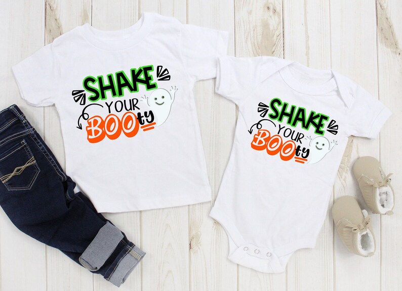 May include: Two white shirts with a ghost graphic and the text "Shake Your Boo-ty" printed on them. One shirt is a long-sleeved t-shirt and the other is a short-sleeved onesie.