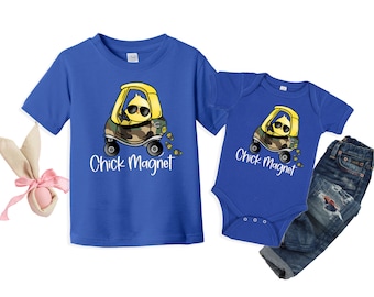 Op de afbeelding: Blauw peuter T-shirt en romper met een afbeelding van een gele kuiken die in een speelgoedauto rijdt en een zonnebril draagt. De tekst "Chick Magnet" staat eronder. Een blauwe jeans met distressed patches is ook inbegrepen.
