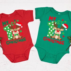 Op de afbeelding: Twee rood-groene korte mouwen onesies met de tekst "My 1st Christmas" en een cartoon rendier met een kerstmanmuts.