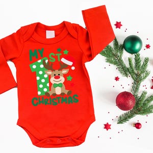 Op de afbeelding: Rode lange mouwen romper met een groen en wit nummer &eacute;&eacute;n, een rendier met een groene strik en de tekst "My 1st Christmas".