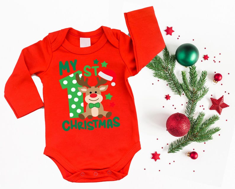 Op de afbeelding: Rode lange mouwen romper met een groen en wit nummer &eacute;&eacute;n, een rendier met een groene strik en de tekst "My 1st Christmas".