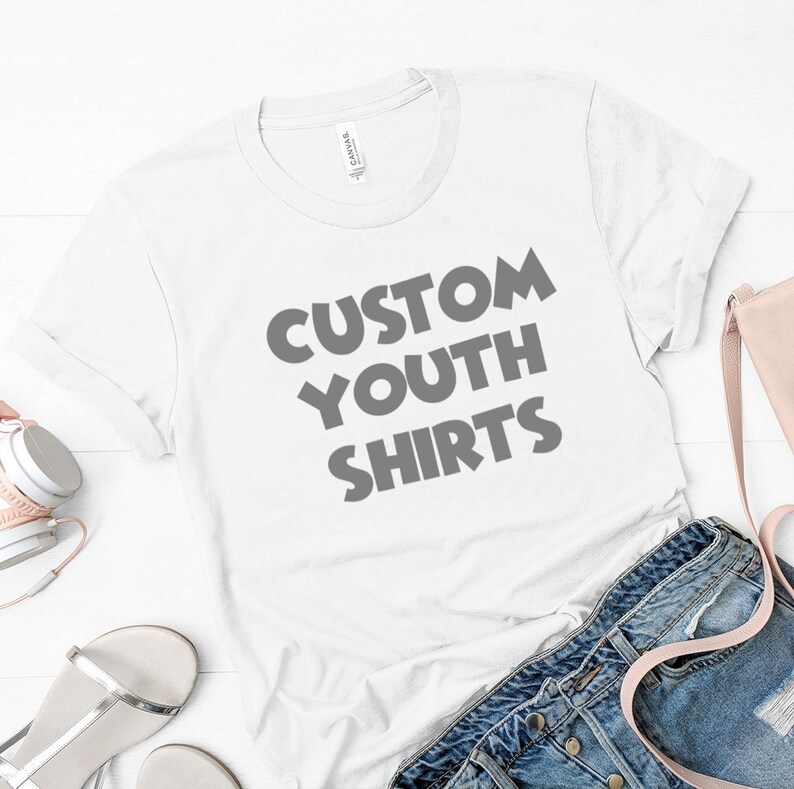Puede incluir: Camiseta blanca con el texto "CUSTOM YOUTH SHIRTS" impreso en gris en la parte delantera.