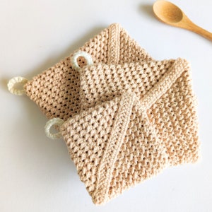 May include: Two crocheted pot holders in a light beige color with white loops. The pot holders are made with a textured stitch pattern.