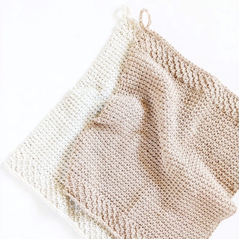 May include: Two crocheted dishcloths, one in a light beige color and the other in a cream color. The dishcloths are made with a simple stitch pattern and have a textured look.