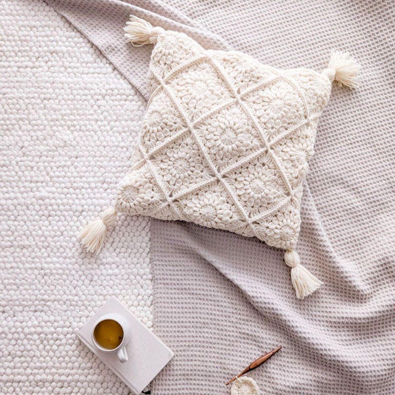 May include: A white crocheted throw pillow with a square pattern and tassels. The pillow is on a light gray textured surface.