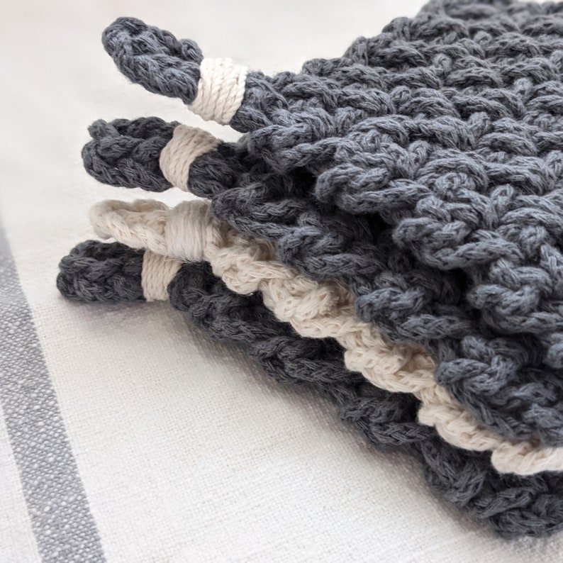 May include: A set of three gray and cream crocheted pot holders. The pot holders are stacked on top of each other, with the gray ones on top and the cream ones on the bottom.
