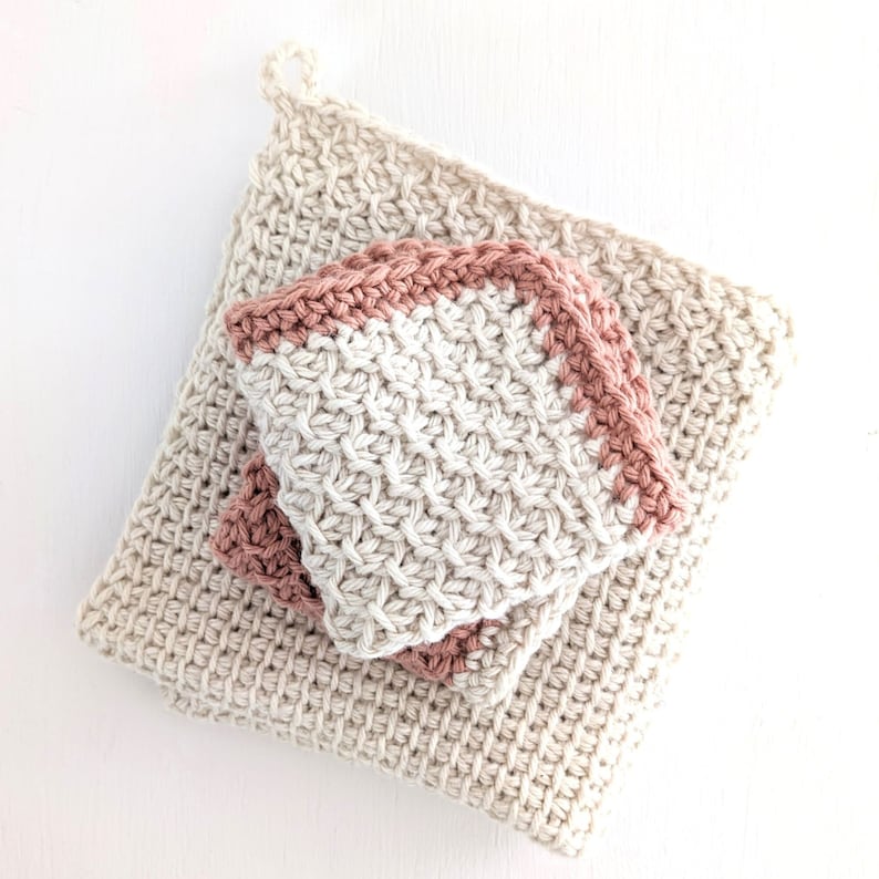 May include: Two crocheted dishcloths, one beige with a pink border and one white with a pink border. The dishcloths are stacked on top of each other.