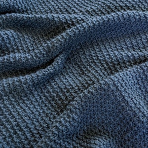 Könnte beinhalten: Nahaufnahme einer blauen Strickdecke mit einem strukturierten Muster. Die Decke ist weich und gemütlich, perfekt zum Kuscheln auf der Couch.