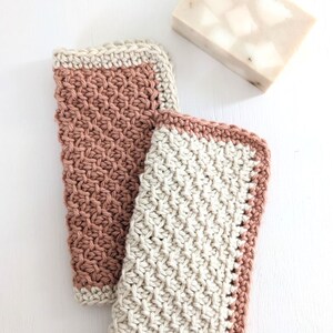 May include: Two crocheted dishcloths, one in a light brown color and the other in a beige color. Both dishcloths have a contrasting border in the opposite color.