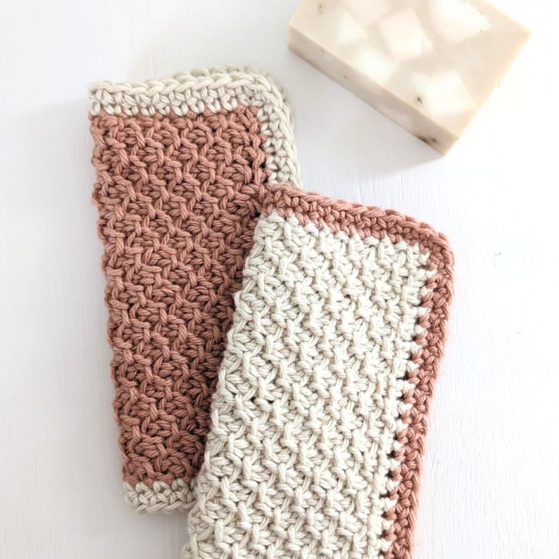 May include: Two crocheted dishcloths, one in a light brown color and the other in a beige color. Both dishcloths have a contrasting border in the opposite color.