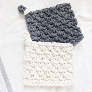 May include: Two crocheted pot holders, one gray and one white, with a woven pattern. The gray pot holder has a loop for hanging.