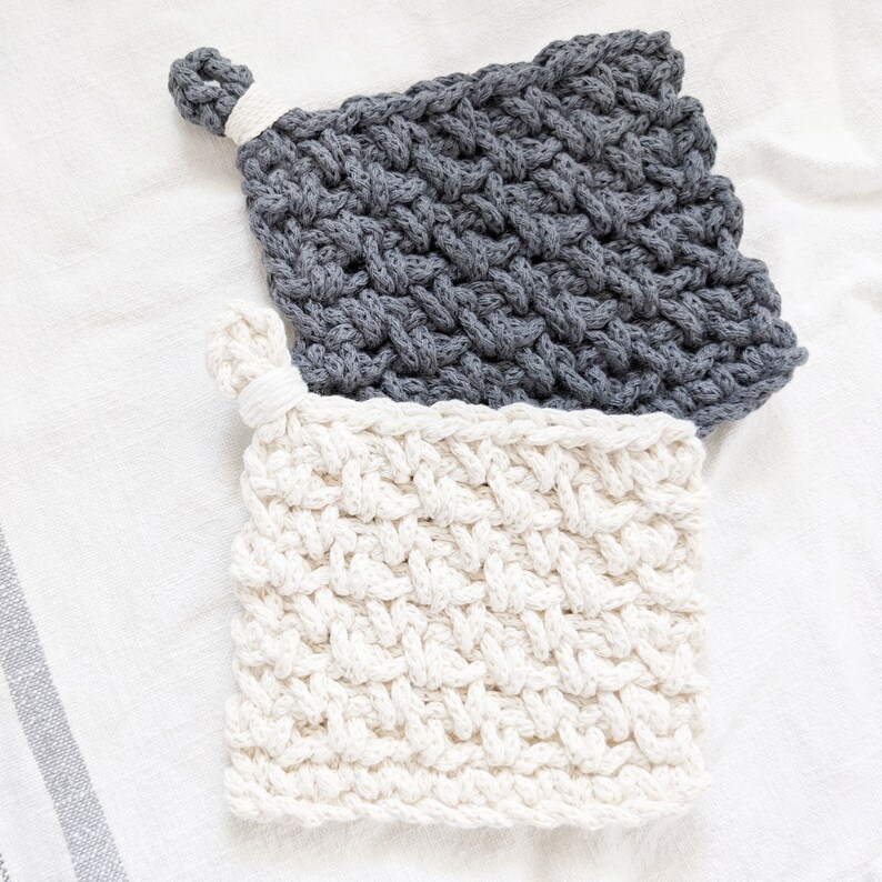 May include: Two crocheted pot holders, one gray and one white, with a woven pattern. The gray pot holder has a loop for hanging.