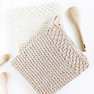 May include: Two crocheted pot holders, one in beige and one in white, are stacked on top of each other. The pot holders are made with a simple stitch pattern and have a textured look.