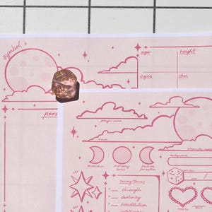 May include: A pink character sheet with a celestial theme, featuring a moon, clouds, and stars. The sheet includes fields for player information and saving throws. A multi-faceted, translucent die rests on the sheet.