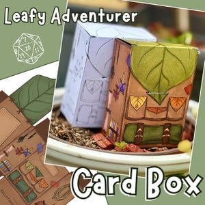 Könnte beinhalten: Eine braune Kartenbox mit einem grünen Blattdesign auf der Oberseite, das einem Rucksack ähnelt. Die Box hat Taschen und Riemen, mit dem Text "Card Box" unten. Die Worte "Leafy Adventurer" stehen oben. Ein weißer und grüner Würfel ist ebenfalls sichtbar.