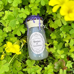 May include: A small glass potion bottle with a label that reads "Bellatores Potion of Invisibility." The bottle has a purple wax seal and is surrounded by green clover and yellow flowers. The potion bottle is filled with a light blue liquid.